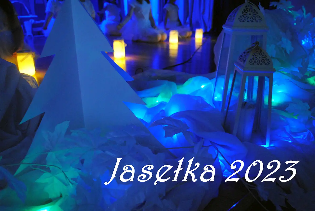 fragment dekoracji (papierowa choinka, latarnie) oświetlonej niebieskim światłem i napis Jasełka 2023