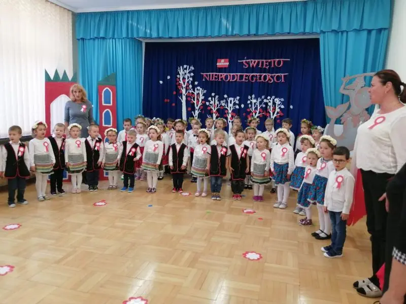 Dzieci z grup Misie i Tygryski w strojach ludowych wraz z nauczycielkami śpiewające hymn
