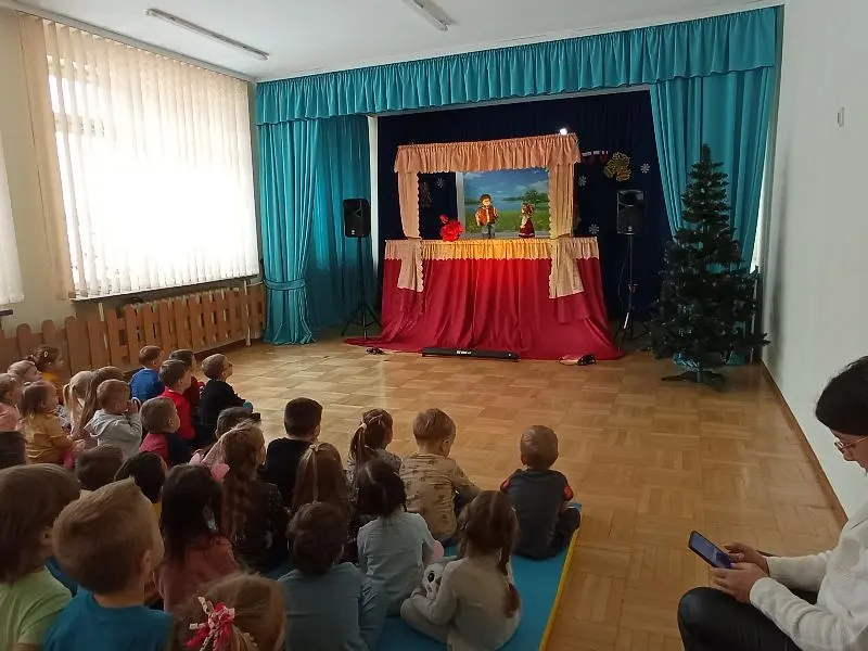 Dzieci zgromadzone w małej auli oglądające przedstawienie teatralne.