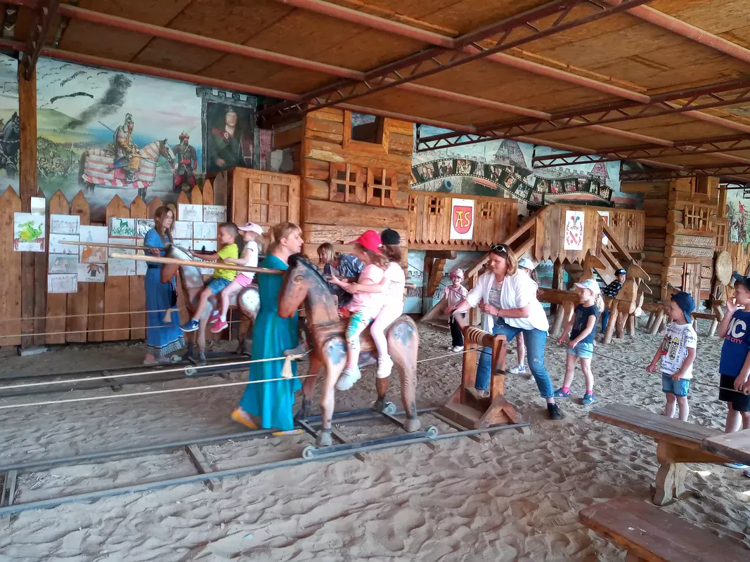 Dzieci wyścigujące się na drewnianych koniach, mechanizm poruszający konie obsługują panie