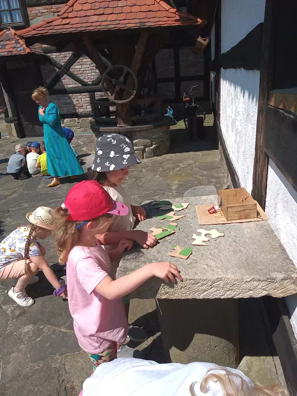 Dzieci w małych grupach wykonują kolejne zadanie – układają drewniane puzzle, na których są cyfry umożliwiające otwarcie drewnianej szkatułki z literami, z których na końcu powstanie imię smoka