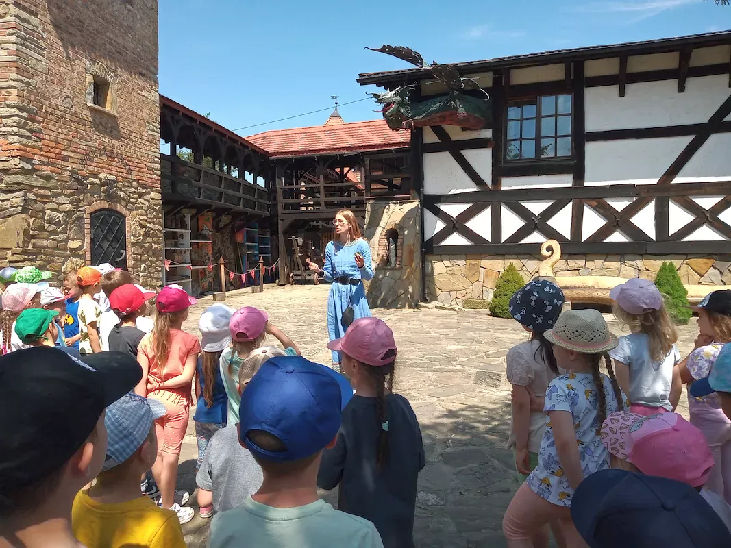Prowadząca opowiada dzieciom o Smoku Grybosie i prezentuje jego postać oplatającą ściany zamku