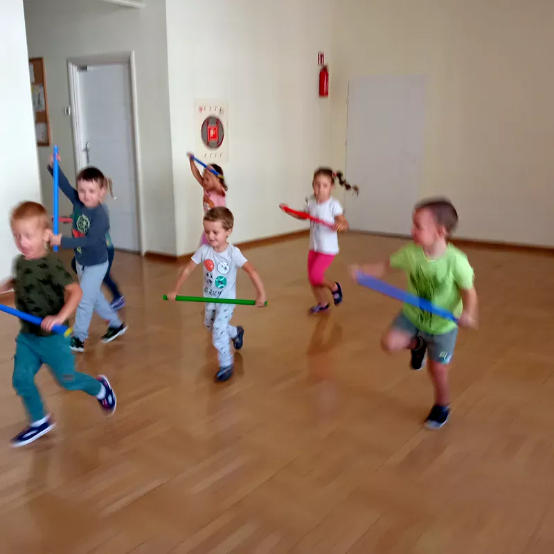 Dzieci w sali gimnastycznej podczas zabawy z laskami