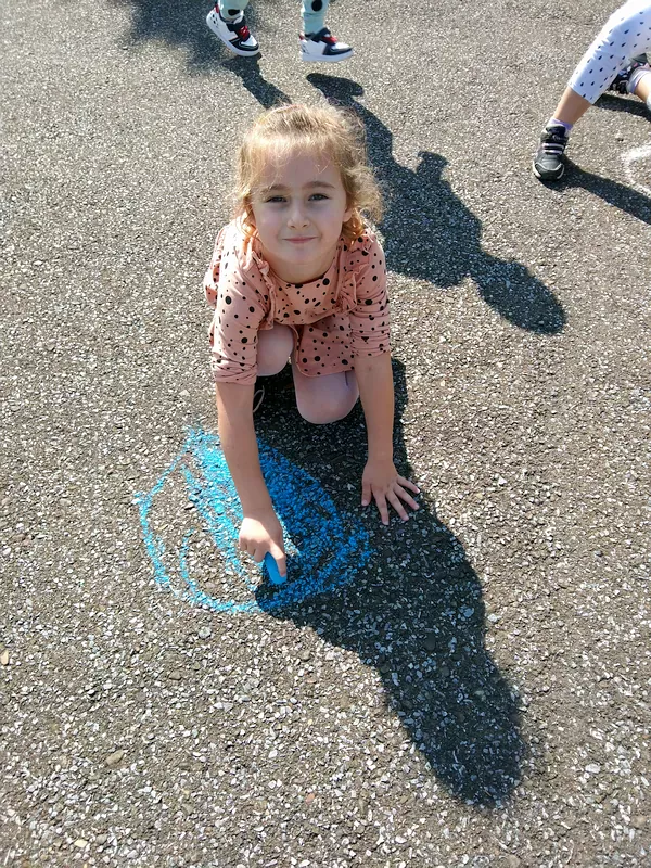 Klara maluje swoją kropkę kredą na betonie.