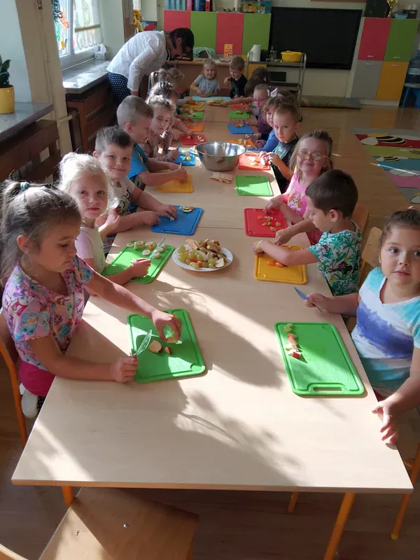 Dzieci przy stolikach kroją owoce