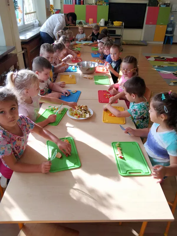 Dzieci przy stolikach kroją owoce