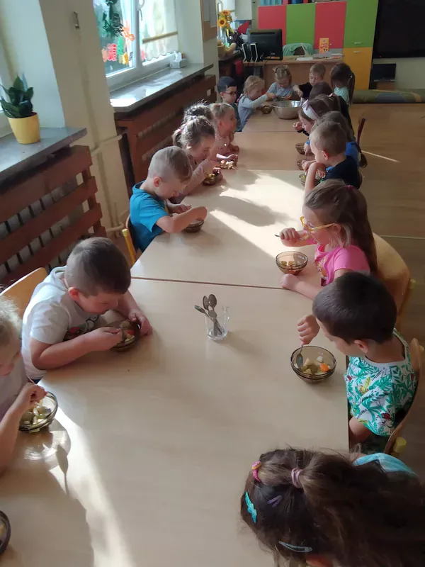 Dzieci przy stoliku jedzą sałatkę owocową