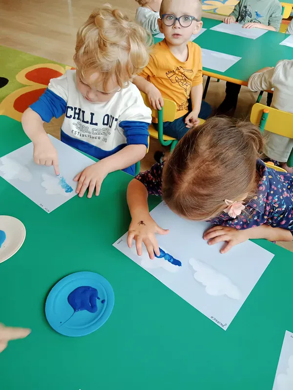 Dzieci malują paluszkami i niebieską farbą chmurki