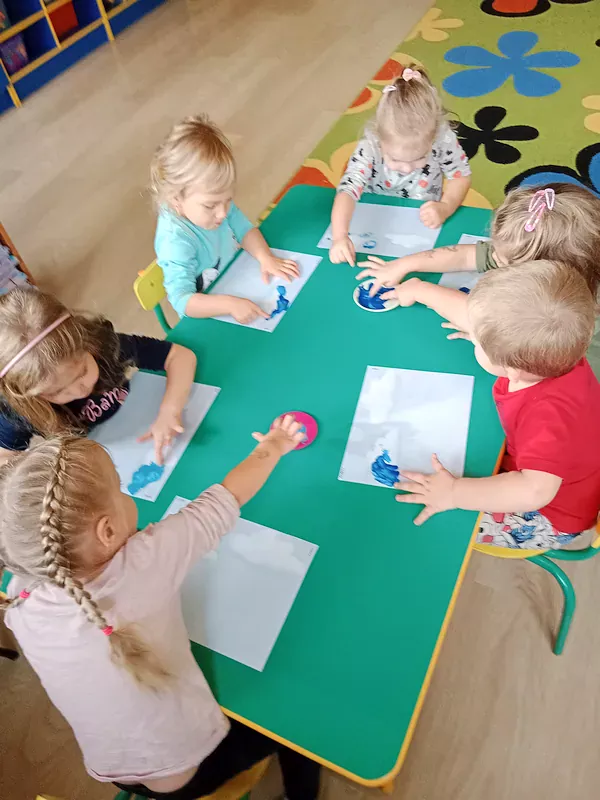 Dzieci malują paluszkami i niebieską farbą chmurki