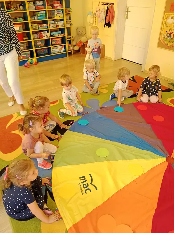 Dzieci podrzucają kolorowe kropeczki na chuście tworząc kolorowy deszczyk