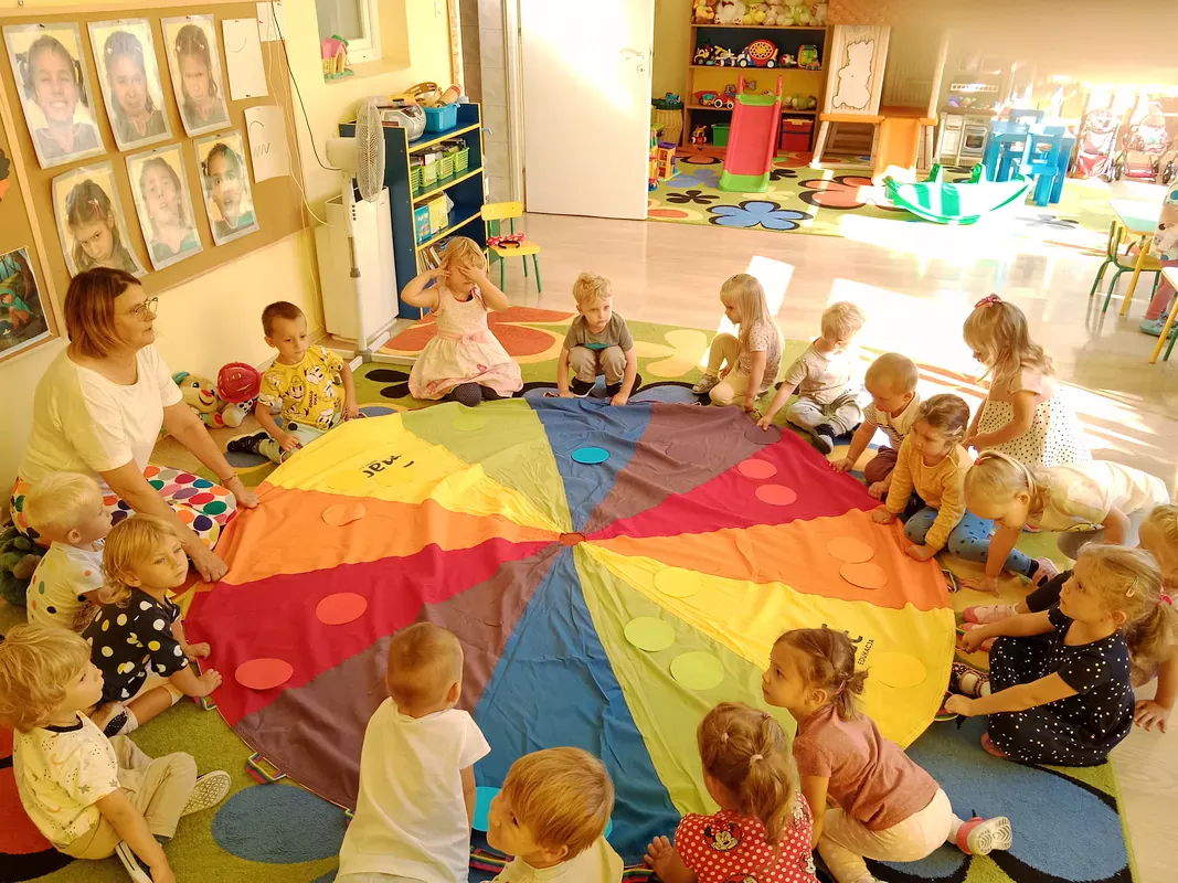 Dzieci podrzucają kolorowe kropeczki na chuście tworząc kolorowy deszczyk