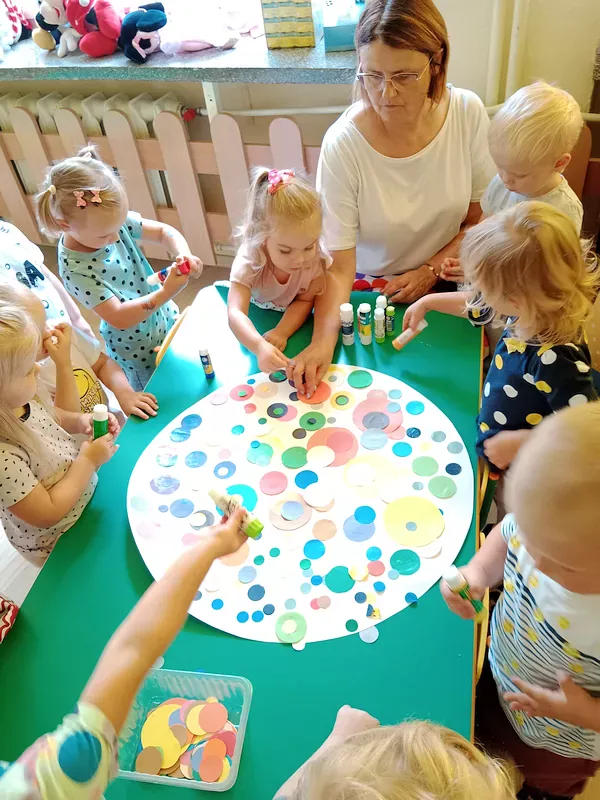 Dzieci wyklejają kropkę XXL z białego brystolu kolorowymi kropeczkami