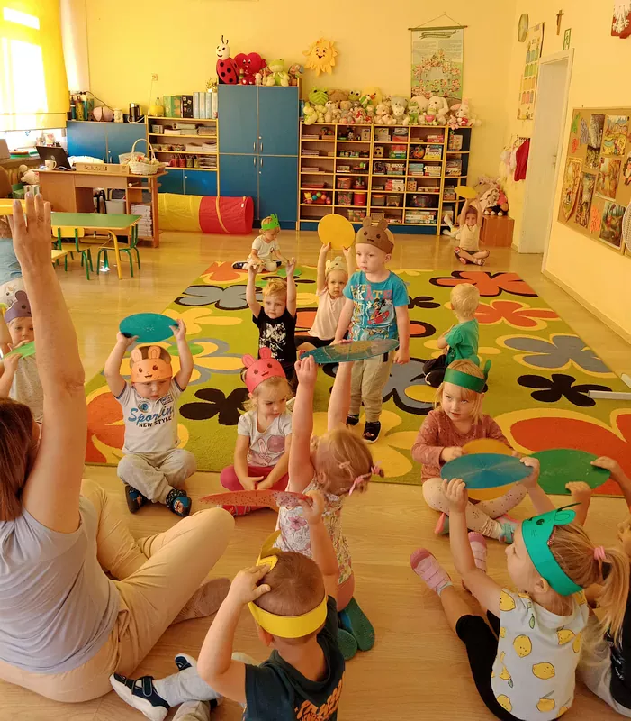 Dzieci siedzą na dywanie z kolorowymi krążkami, podnoszą nad głową