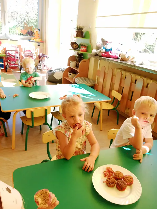 Dzieci siedzą przy stolikach i zajadają muffinki