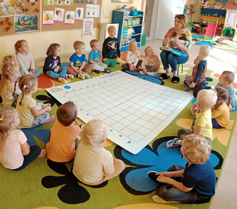 Dzieci siedzą wokół maty, nauczycielka prezentuje robota