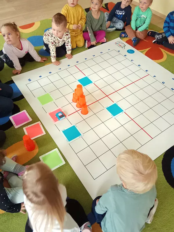 Dzieci przyglądają się jak zachowuje się zakodowany robot omijający wieżę z kubków