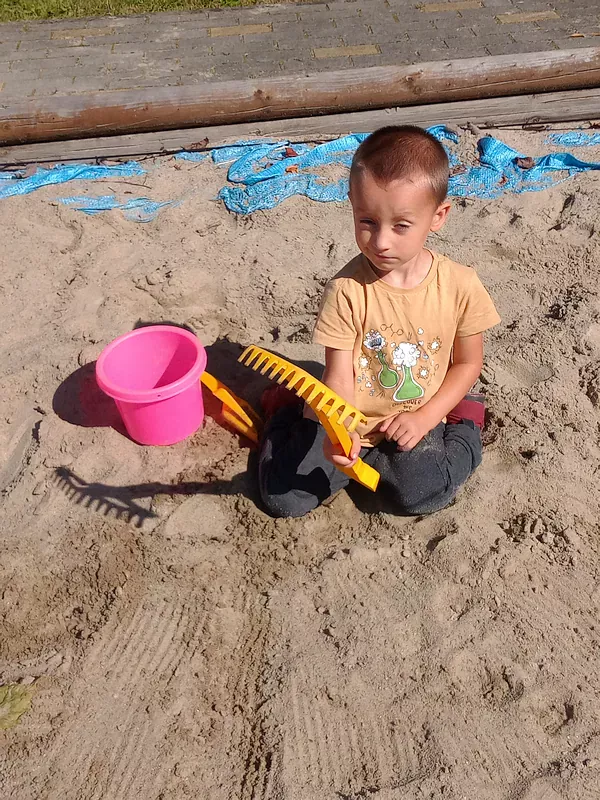 Krystian bawi się w piaskownicy grabkami-grabi piasek