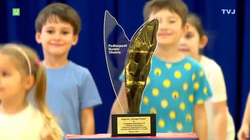 kadr z programu TVJ: w tle uśmiechnęte dzieci, na pierwszym planie satuetka Nagrody „Złotego Prymu”